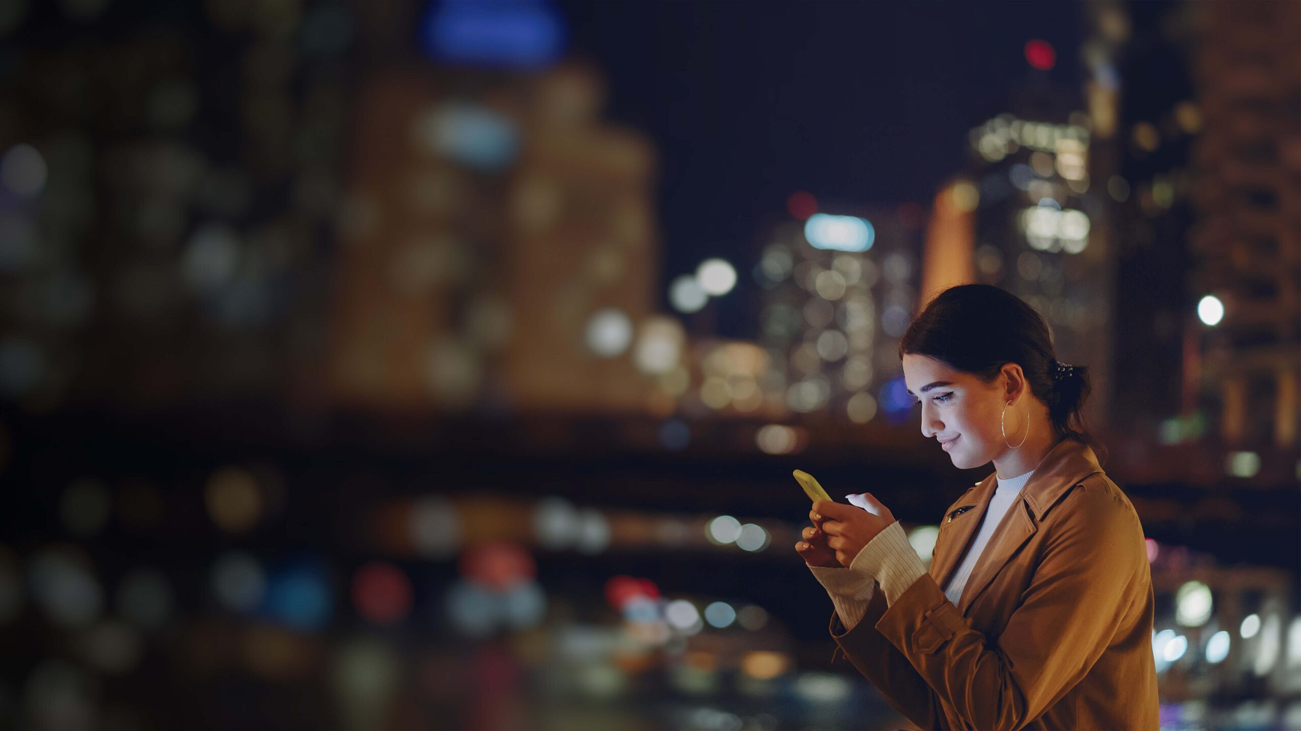 A woman is using her cell phone in a city at night.