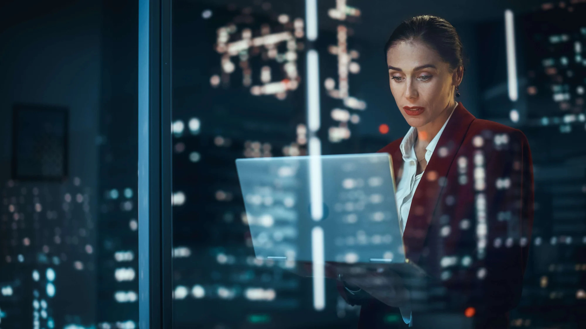 A woman in a business suit is using a laptop at night.