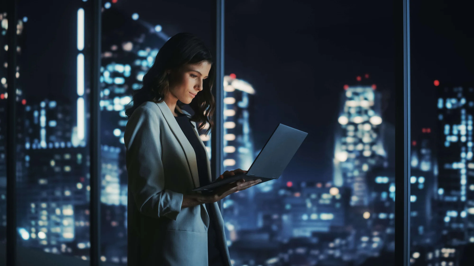 A business woman using a laptop in a city at night.