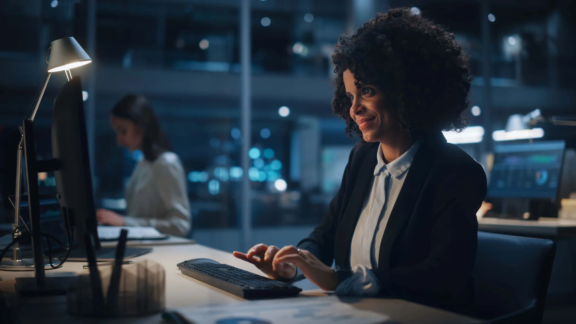 A woman working at a computer desk at night.