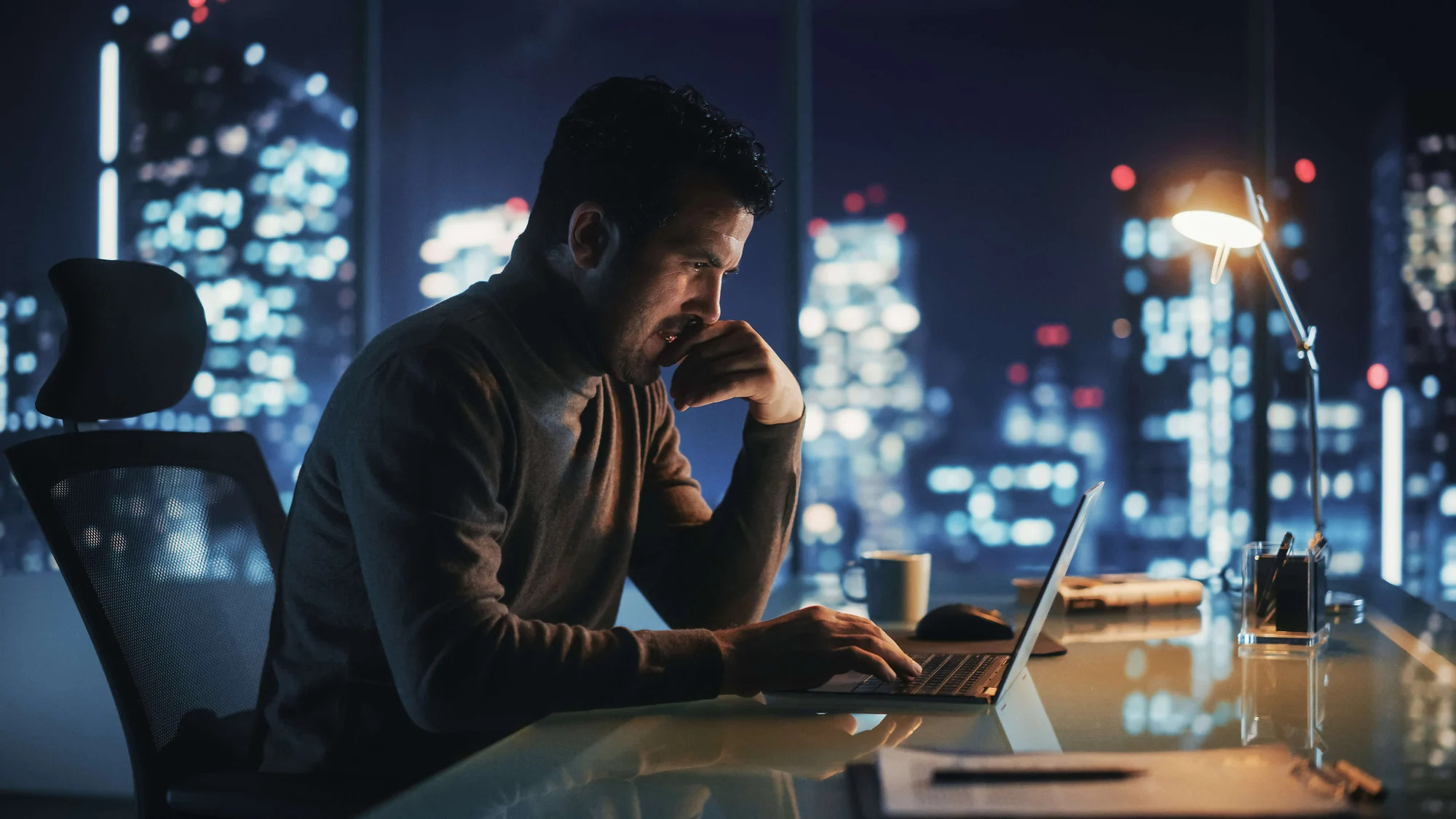 A man working on a laptop in front of a city at night.