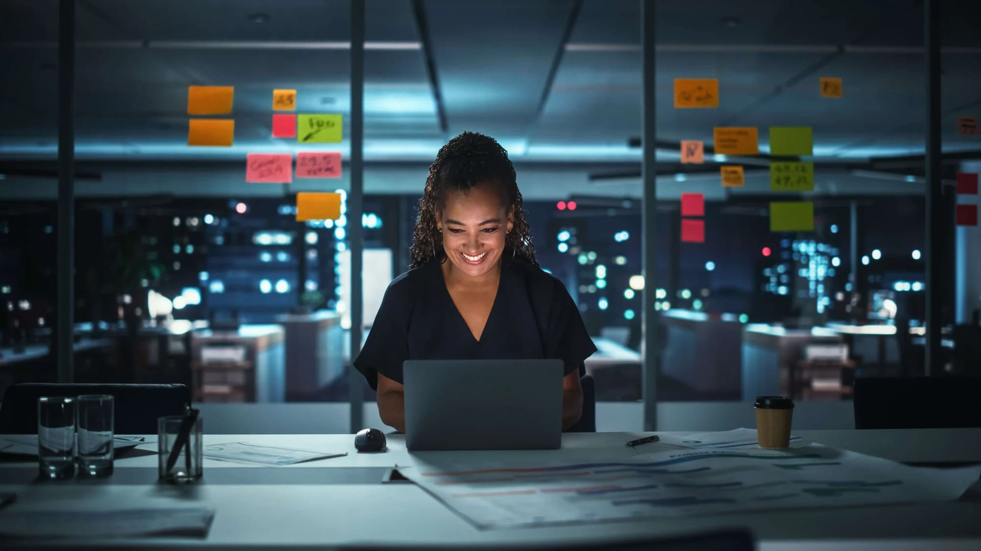 A woman is sitting at a desk with a laptop in front of her.