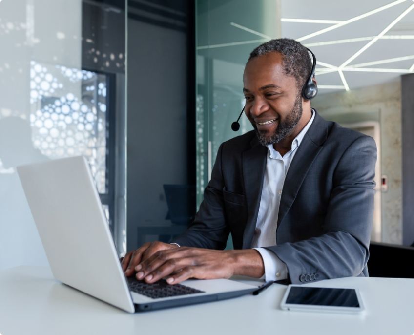 A man wearing a headset is working on a laptop.